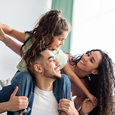 family with child on parent's shoulders smiling 