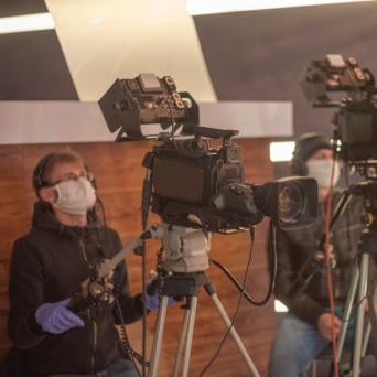 man wearing a medical mask operating a professional film camera