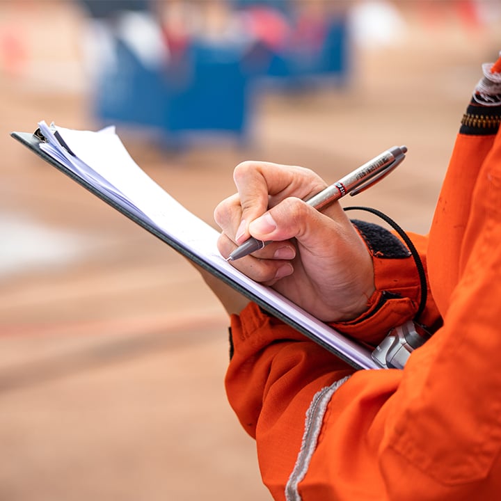 person's hand writing on a clipboard while wearing an orange coat