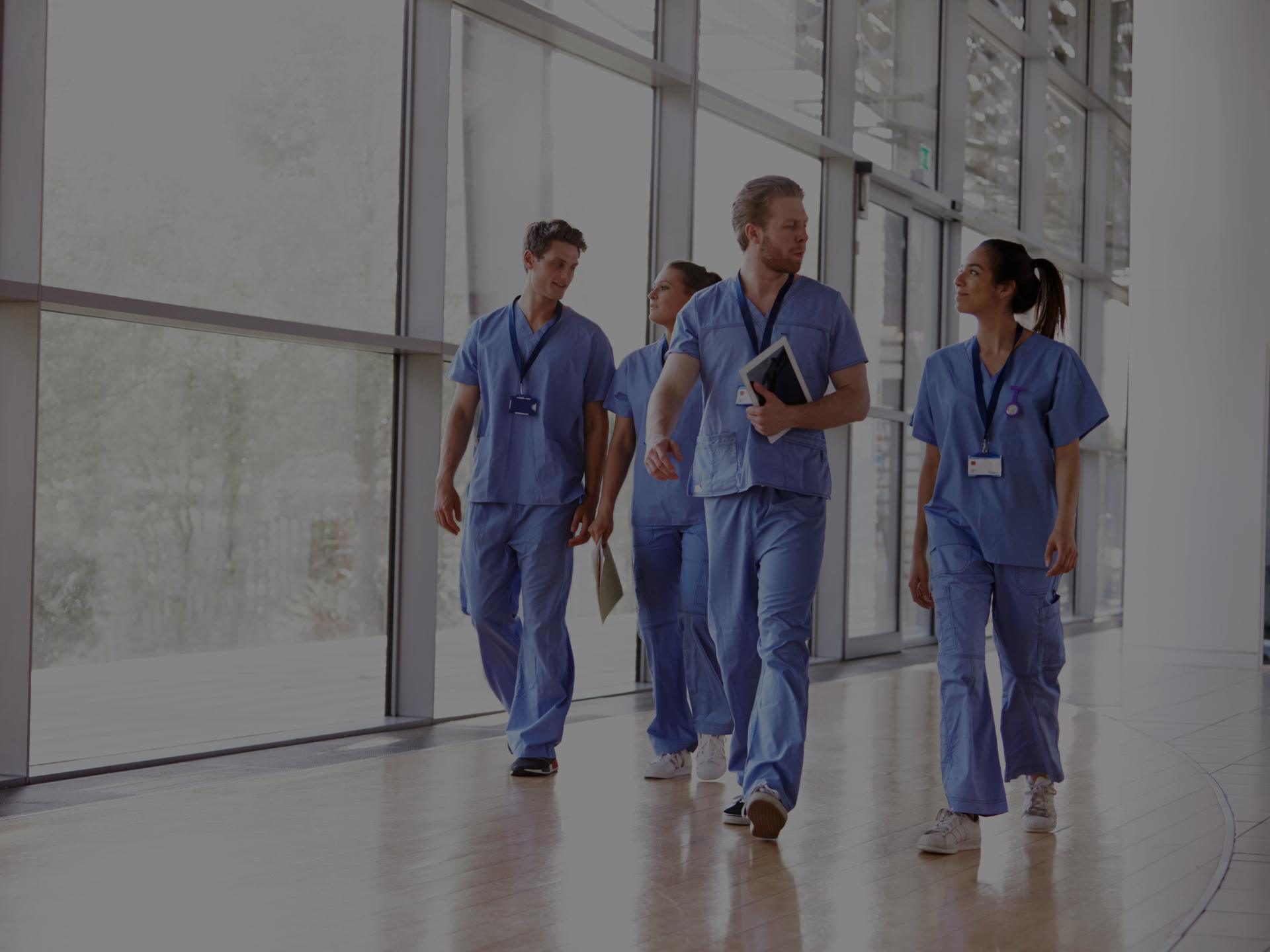 Nurses in scrubs walking together in hospital hallway.